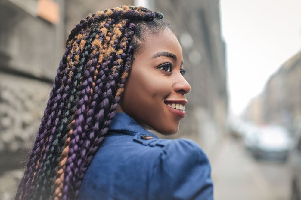 mujer sonriente de perfil con trenzas afro violetas